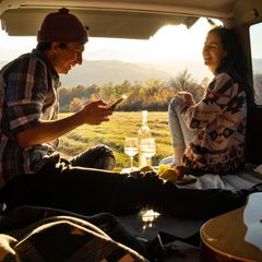 Ein Paar sitzt an der Öffnung des Kofferraums und trinkt Wein