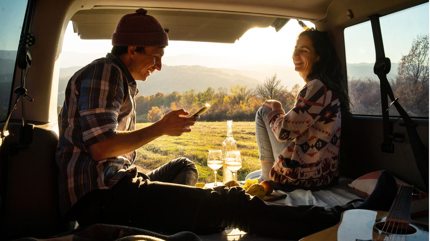 Camping mit dem Auto Ein Paar sitzt an der Öffnung des Kofferraums und trinkt Wein