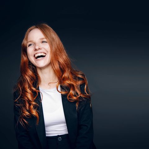 Eine rothaarige Frau mit großem Lachen vor einem dunklen Hintergrund