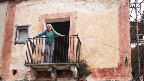 Eine Frau steht auf dem Balkon ihres heruntergekommenen italienischen Häuschens