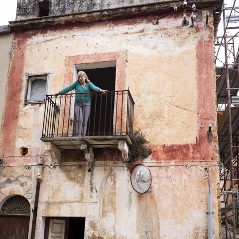 Eine Frau steht auf dem Balkon ihres heruntergekommenen italienischen Häuschens