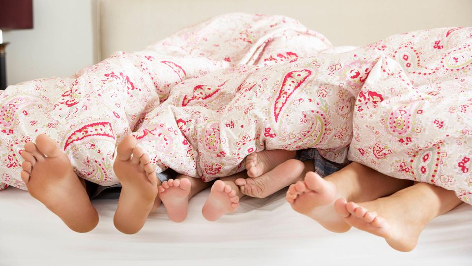 Füße einer Familie ragen aus der Bettwäsche Füße einer Familie ragen aus der Bettwäsche