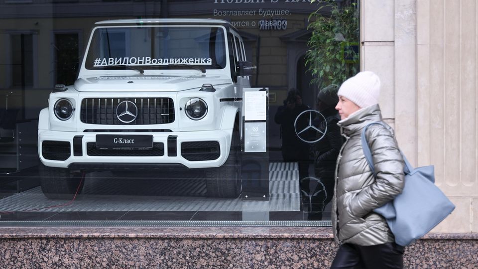 Eine Frau geht vor einem Mercedes-Benz-Autohoaus in Moskau spazieren, im Schaufenster ein weißer Mercedes