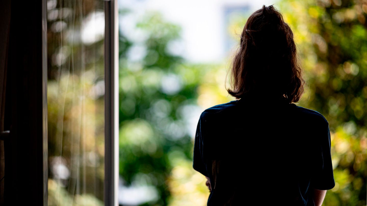 Eine junge Frau schaut aus dem geöffneten Fenster ins Grüne