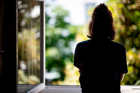 Eine junge Frau schaut aus dem geöffneten Fenster ins Grüne