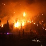 Ein Waldbrand am McDougall Creek erhellt die Nacht an einem Berghang in West Kelowna. Die Größe des Feuers wird klar, wenn man sich das beleuchtete Haus rechts unten im Bild anschaut