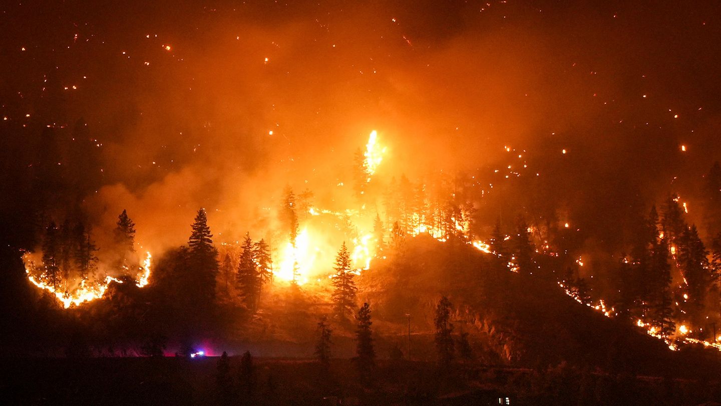 Ein Waldbrand am McDougall Creek erhellt die Nacht an einem Berghang in West Kelowna. Die Größe des Feuers wird klar, wenn man sich das beleuchtete Haus rechts unten im Bild anschaut