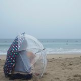 Auch am berühmten Venice Beach trotzt eine Person dem Wetter, sitzt mit Regenschirmen im Sand und beobachtet Surfer.