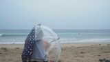 Auch am berühmten Venice Beach trotzt eine Person dem Wetter, sitzt mit Regenschirmen im Sand und beobachtet Surfer.