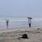 Am Imperial Beach in Kalifornien stehen Frauen im Regen und halten das stürmische Wetter mit ihren Handys fest.