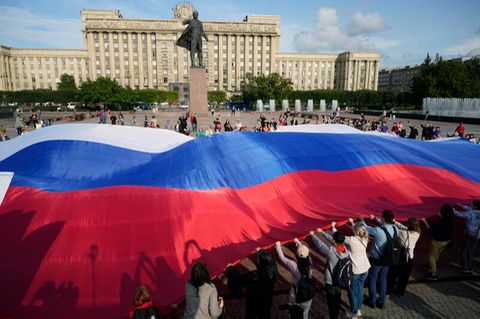 St. Petersburg, Russland. Menschen halten eine riesige russische Nationalflagge neben einer Lenin-Statue anlässlich des Nationalflaggentags.