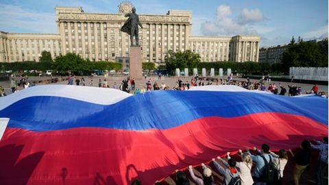 St. Petersburg, Russland. Menschen halten eine riesige russische Nationalflagge neben einer Lenin-Statue anlässlich des Nationalflaggentags.