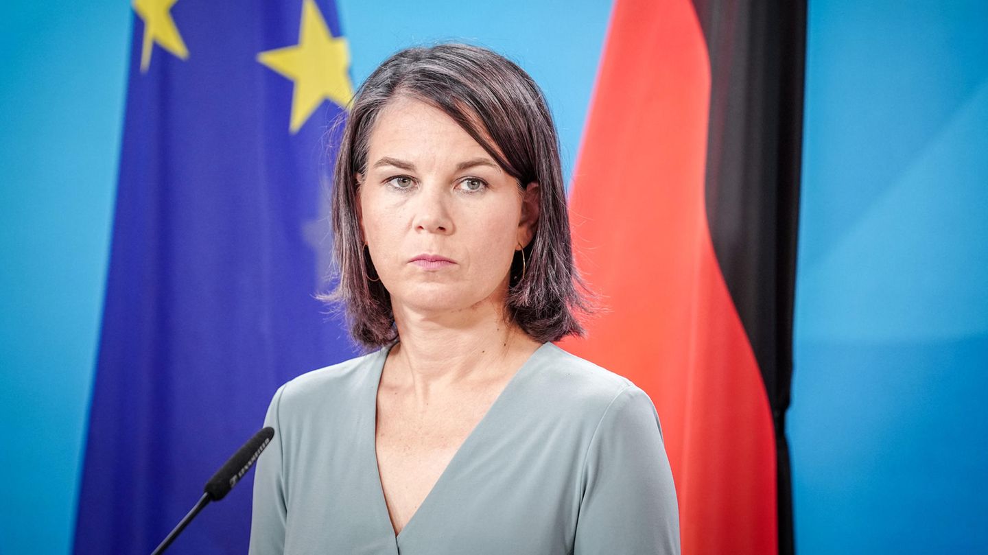 Annalena Baerbock steht vor einer Europa- und einer Deutschland-Flagge an einem Mikro und schaut ernst
