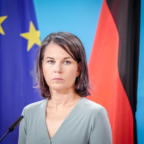 Annalena Baerbock steht vor einer Europa- und einer Deutschland-Flagge an einem Mikro und schaut ernst