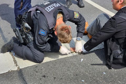 Ein Polizist versucht die Hand eines Aktivisten von der Straße zu lösen