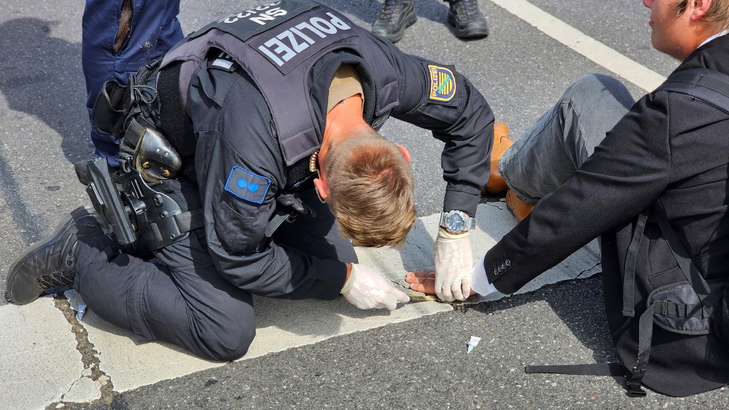 Ein Polizist versucht die Hand eines Aktivisten von der Straße zu lösen Ein Polizist versucht die Hand eines Aktivisten von der Straße zu lösen