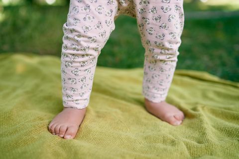 Die Beine eines Babys stehen auf einer grünen Decke
