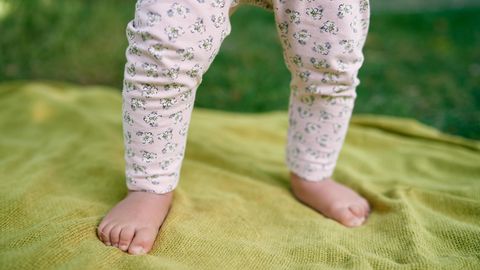 Die Beine eines Babys stehen auf einer grünen Decke