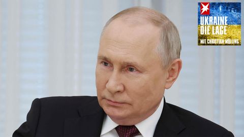 Wladimir Putin sitzt in Anzug und Krawatte da und lächelt leicht