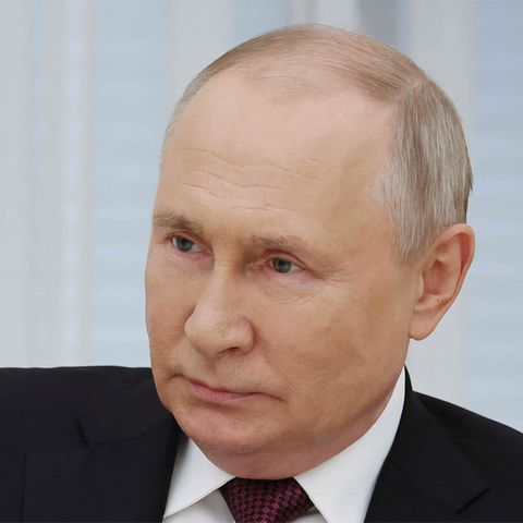 Wladimir Putin sitzt in Anzug und Krawatte da und lächelt leicht