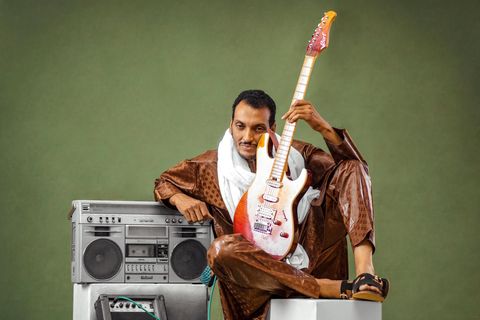 Ein Mann sitzt mit E-Gitarre neben einer Stereoanlage