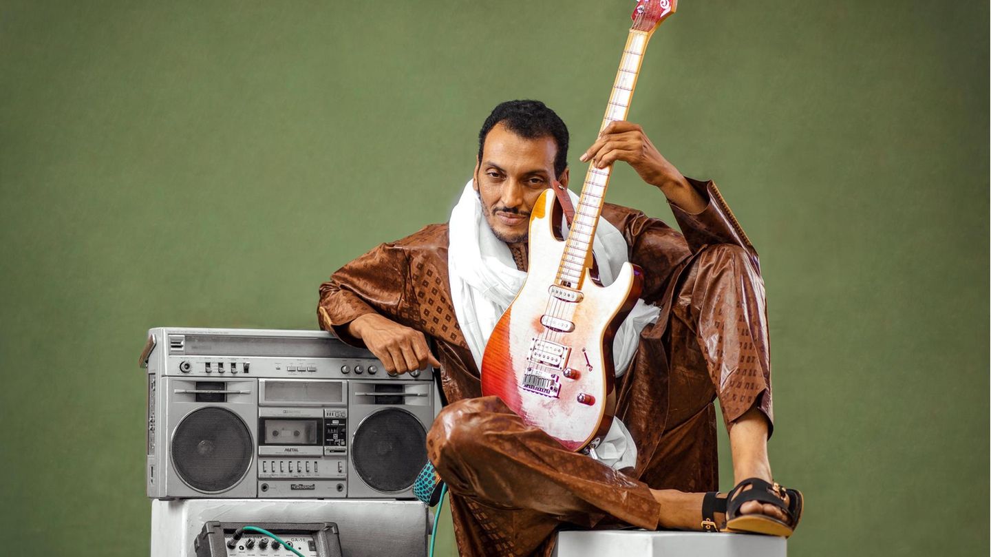 Ein Mann sitzt mit E-Gitarre neben einer Stereoanlage