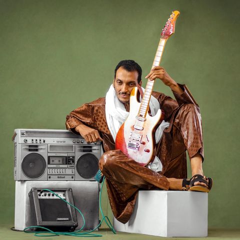 Ein Mann sitzt mit E-Gitarre neben einer Stereoanlage