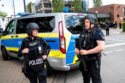 Eine Polizistin und ein Polizist der Polizei Hamburg stehen in Schutzwesten und Helmen neben einem Mannschaftswagen