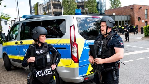 Eine Polizistin und ein Polizist der Polizei Hamburg stehen in Schutzwesten und Helmen neben einem Mannschaftswagen
