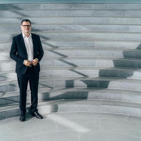 Wolgang Schmidt steht im Anzug vor Treppen