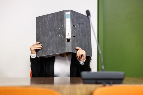 Eine Angeklagte hält sich im Gerichtssaal vom Oberlandesgericht einen Aktenordner vors Gesicht