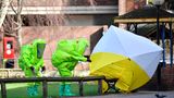 Zwei Menschen in grünen Schutzanzügen und ein Sichtschutz vor der Parkbank