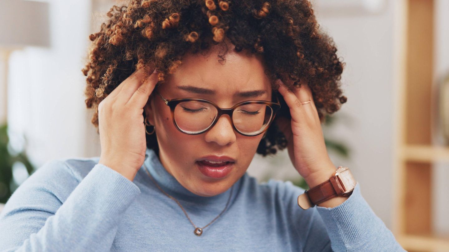 Long Covid: Eine Frau reibt sich mit geschlossenen Augen die Schläfen und sieht matt und müde aus