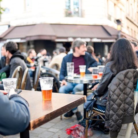 Vor einem Pariser Café sitzen Menschen mit Bier