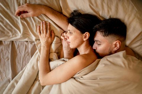 Ein Paar liegt im Bett. Er umarmt sie von hinten.