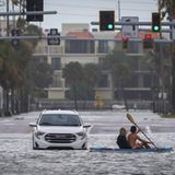 Ein Mann und eine Frau fahren mit dem Kajak an einem verlassenen Fahrzeug vorbei