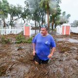 Ein Mann watet durch das Wasser vor seinem Haus
