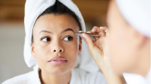 Eine Frau zupft sich die Augenbrauen mit einer Pinzette.