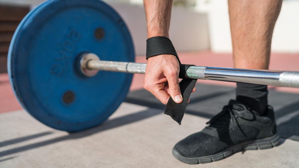 Zughilfen im Krafttraining: Mann fixiert Zughilfen an einer Hantelstange