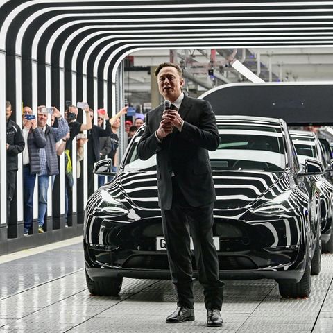 Elon Musk mit Mikro vor einem schwarzen Tesla bei einer Veranstaltung