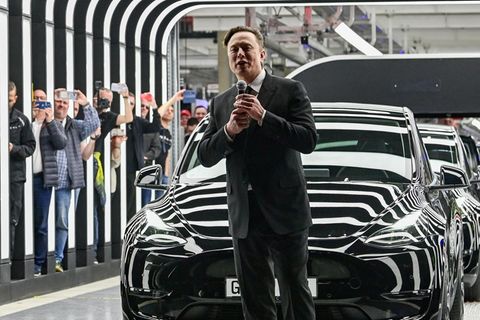 Elon Musk mit Mikro vor einem schwarzen Tesla bei einer Veranstaltung
