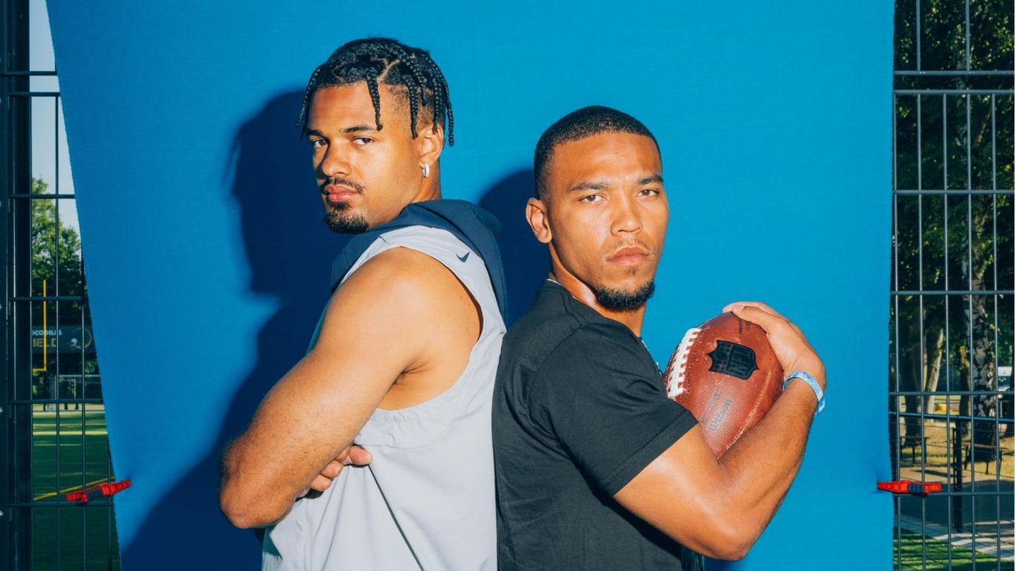 Equanimeous und Amon-Ra St. Brown stehen mit dem Rücken gegeneinander gelehnt vor einer blauen Matte