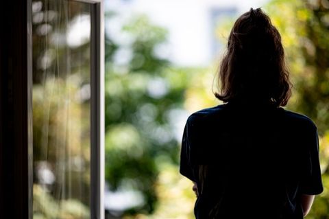 Eine Frau steht in ihrer Wohnung am Fenster