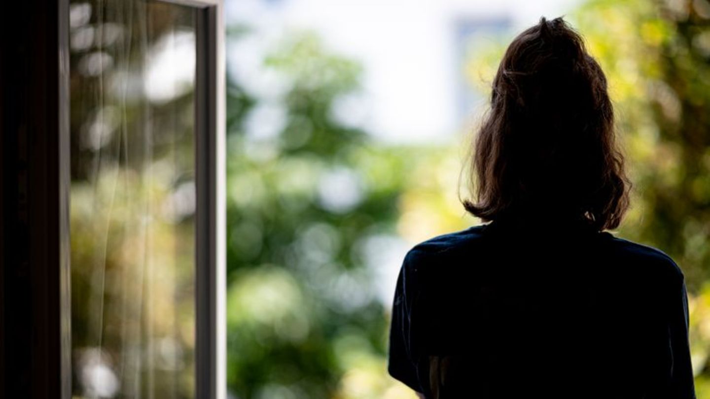 Eine Frau steht in ihrer Wohnung am Fenster