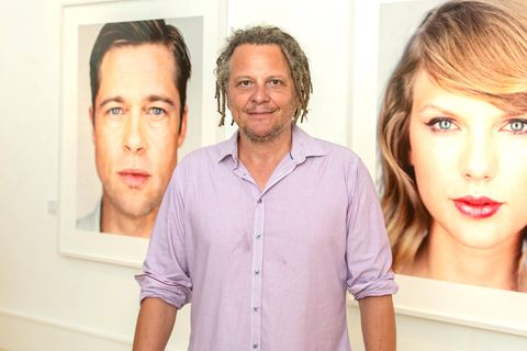 Martin Schoeller, ein Mann mit kurzen Dreadlocks, steht zwischen zwei seiner Fotos. Sie zeigen Brad Pitt und Taylor Swift