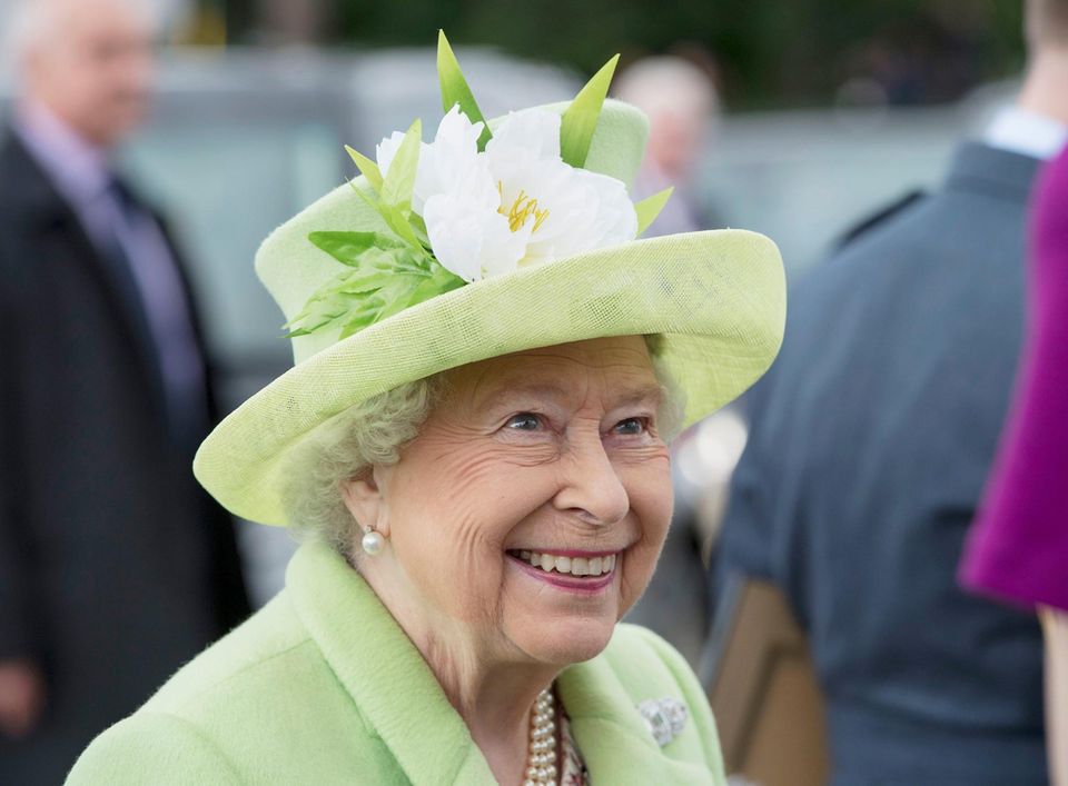 The Queen laughs. She wears a light green hat with a white flower on it The Queen laughs. She wears a light green hat with a white flower on it