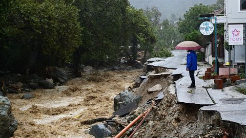 Eine Person blickt von einer zerstörten Straße in Griechenland auf Überschwemmungen
