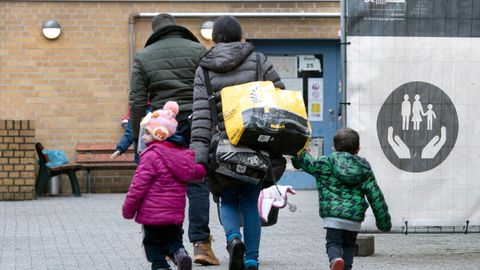 Eine Mutter trägt zwei Taschen und geht mit ihren beiden Kindern zu einer Aufnahmeeinrichtung für Flüchtlinge