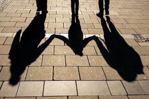 Die Schatten von zwei Erwachsenen und einem Kind fallen in den Morgenstunden auf den Asphalt