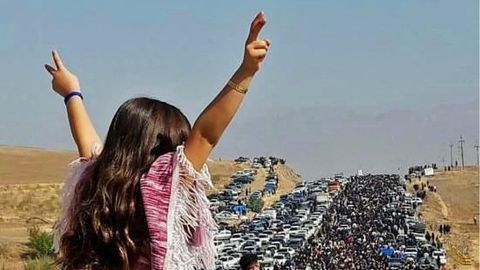 Eine Frau im Iran steht ohne Kopftuch auf einem Auto und macht mit beiden Händen ein Victory-Zeichen